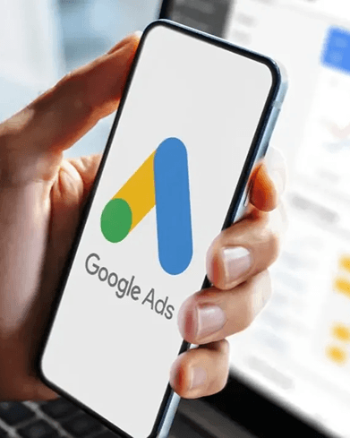 Hand holding a phone showing the Google Ads logo, with a Google search results page in the background